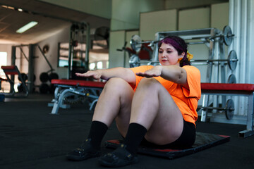 Beautiful young adult overweight Latina woman exercising, doing crunches at a gym, pushing herself...