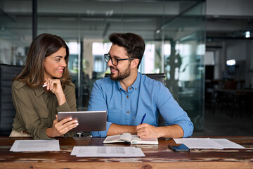 Fototapeta na wymiar Two happy busy business people man and woman talking using digital tablet in office. Smiling professional colleagues at having conversation working together with tab tech at corporate meeting.