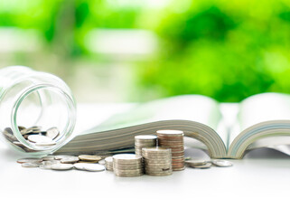 An open book and a jar of coins sit next to a small pile of loose change.