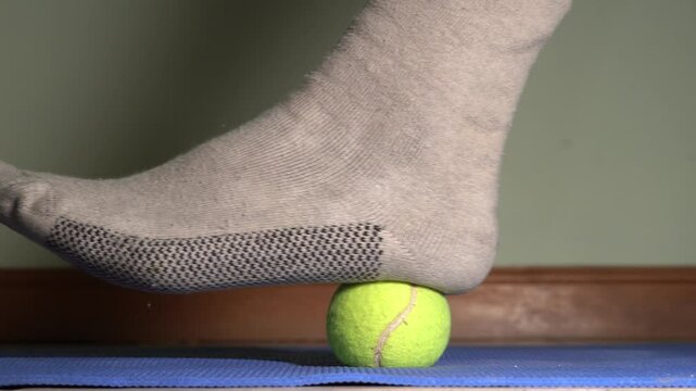 Plantar fasciitis massage using a tennis ball on a yoga mat