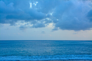 Ocean Waves Under Heavily Cloudy Sky : A wide view of the ocean with waves breaking on the shore under a heavily cloudy, almost overcast sky.