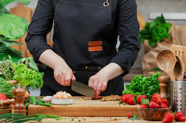 Chef cooking food in the kitchen. Cook chops dry walnuts, prepare yummy salad. Wooden table, kitchenware, vegetables, herbs and ingredients. Healthy vegan eating, recipes, blogging