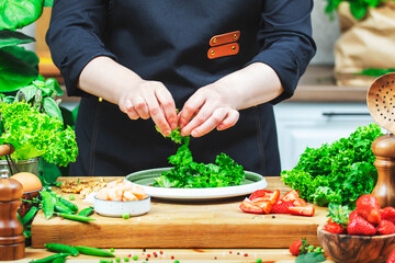 Chef cooking food in the kitchen. Cook prepares gourmet lettuce salad with strawberries and shrimp., wooden table with kitchenware, vegetables, herbs and ingredients. 