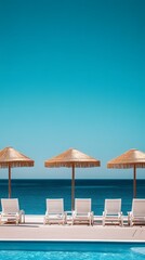 White lounge chairs and straw umbrellas by a swimming pool overlooking the ocean.