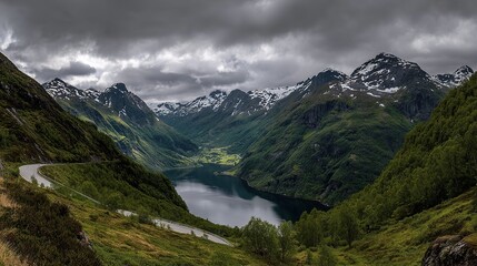 A bird's-eye view of the fjord, surrounded by towering mountains, green valley walls and a winding road leading to snow-capped peaks in the distance, offers panoramic views.