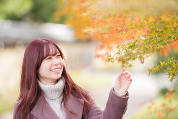On a cold December morning, a Japanese woman in her early twenties with long pink hair, in a pink trench coat, strolls slowly through a traditional town, gently admiring the autumn colors around her.