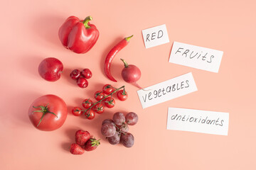 Red fruits and vegetables and corresponding inscriptions on white paper close-up view from above