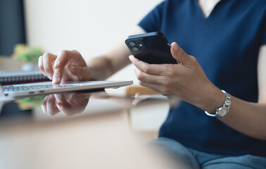 Business woman using smartphone, working on laptop computer at coffee shop or home office. Casual woman using smartphone and laptop browsing the internet or social networking at cafe, remote work