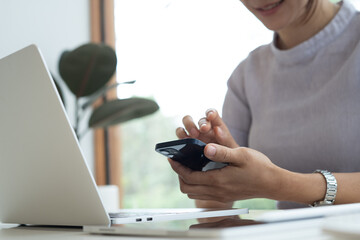 Fototapeta premium Woman using smartphone during working on laptop computer at coffee shop or home office. Casual business woman using smartphone and laptop browsing the internet or social networking, remote work