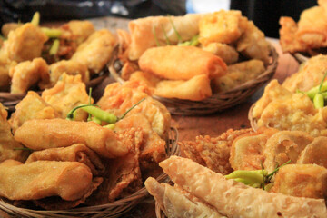 Woven baskets filled with various types of golden-brown fried snacks, including spring rolls, tofu, garnished with green chilies. Represent food, Indonesian cuisine, street food, or a market stall