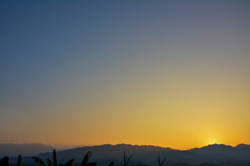 Sunrise Over Silhouetted Mountains: A view of the sun rising over the dark silhouettes of mountains against a gradient sky of blue, orange, and yellow.