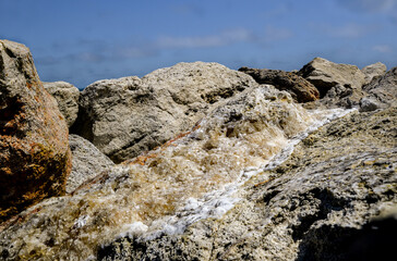 Weathered Coastal Rocks with Mineral Veins Under Bright Blue Sky