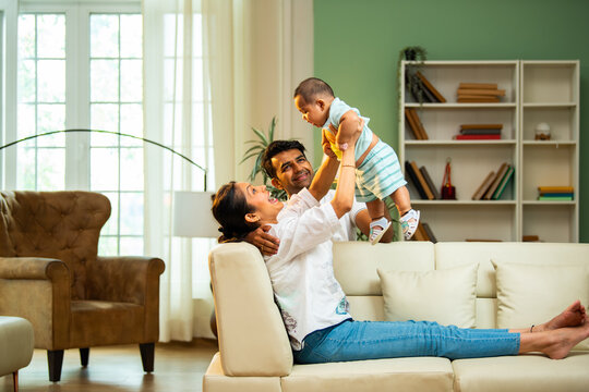 Parents catch baby boy while sitting on sofa at home, enjoying fun playful family bonding time - Powered by Adobe