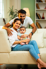 Young Indian couple sitting with baby boy indoors showing care, happiness, modern family lifestyle