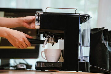 Barista grinding coffee beans and pouring espresso from machine in café, showing close-up of professional preparation of hot aromatic drink.