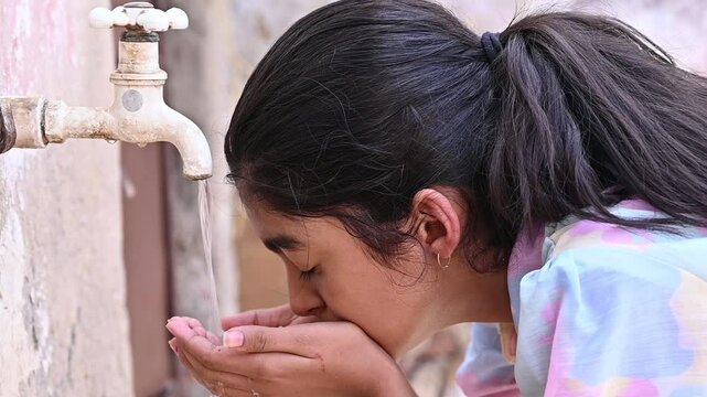 Indian Girl Child Drinking Fresh safe and  Clean Water From Tap in  hot summer day,  hygiene, improved living conditions in rural India. 