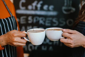 Two friends clink coffee mugs in a cozy café, enjoying a warm beverage together, symbolizing friendship, relaxation, and shared moments.