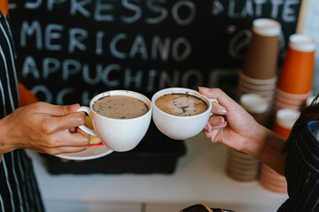 Two friends clink coffee mugs in a cozy café, enjoying a warm beverage together, symbolizing friendship, relaxation, and shared moments.
