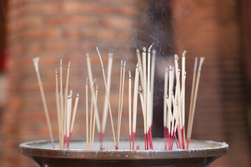 Incense sticks are stuck in a pot with smoke rising from above. Incense sticks that are lit to...