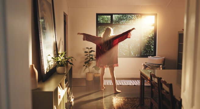 Back, woman and stretching arms by window in home for freedom, peace and ready to start day in house. Sunshine, good morning and person with view for wake up, flare and fresh with energy on weekend