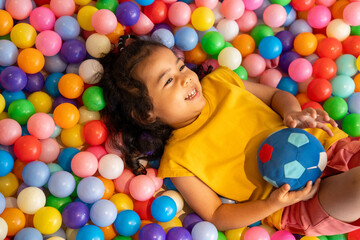 Obraz premium A happy little girl plays with a ball in a colorful ball pit, enjoying the fun and enhancing her development through playful activities and exercise.