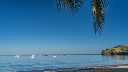 Beautiful serene seascape. A sunny day. White boats in the blue ocean. Sandy beach. A hill in the distance. Green palm leaves against a clear azure sky. Copy space. Madagascar.  Nosy Be 