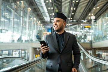 Muslim asian businessman traveler holding boarding pass ticket, passport and smartphone at the airport terminal with luggage. Cheerful tourist islamic at airport holiday trip.