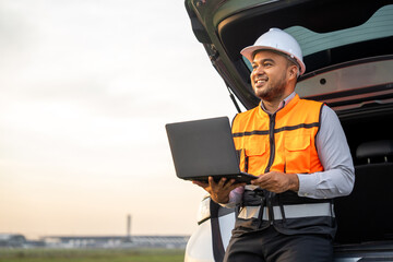 Smart engineer wearing safety uniform working with laptop sitting back of the car near airport at...