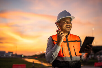 Smart engineer wearing safety uniform working with tablet near airport at night. Maintenance...