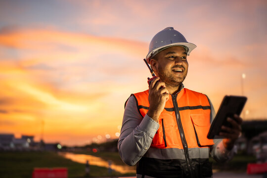Smart engineer wearing safety uniform working with tablet near airport at night. Maintenance Engineer using tablet to checking inspection in night lights of industry background