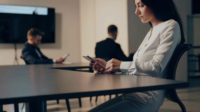 Bored office worker secretly uses phone under table during meeting. Colleagues blurred in background. Neutral tones, corporate setting, discreet behavior.