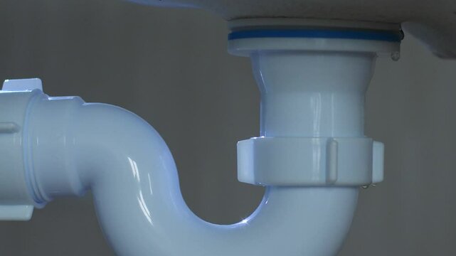 water leak in the bathroom from the siphon close-up, with the light of a flashlight in the bathroom they are looking for a leak from the sewer pipes, repair of the plumbing in the house