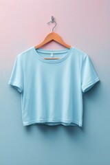 A light blue cropped t-shirt mockup hanging on a wooden hanger against a gradient pink and blue background.