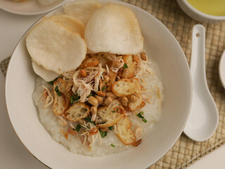 Rice porridge in a bowl, served with shredded chicken, chicken stock, fried shallot and crackers