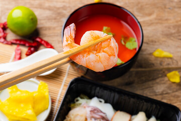 Chopsticks with fresh shrimp, seafood food with noodles and soup, close-up