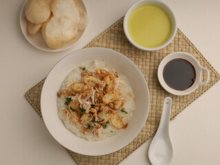 Rice porridge in a bowl, served with shredded chicken, chicken stock, fried shallot and crackers