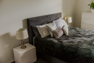 Pillows on double bed with black blanket next to two lamps on bedside tables