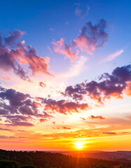 Fototapeta premium A vibrant sunset with colorful clouds fills the sky above a dark, tree-lined horizon, creating a dramatic and peaceful landscape