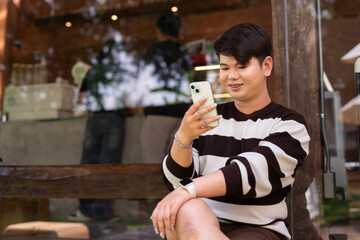 Portrait of a young gay man sitting outside of cafe restaurant during summer