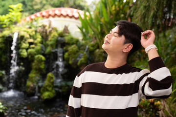 Portrait of a young gay man outdoors at traditional Zen garden with waterfall 