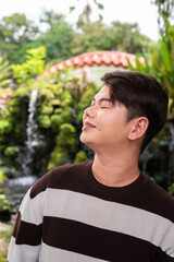 Portrait of a young gay man outdoors at traditional Zen garden with waterfall 