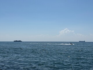 A vast expanse of blue ocean under a clear sky, with a large cargo ship visible on the horizon. 