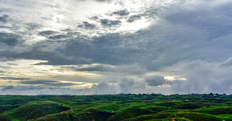 Green undulating hills under a dramatic, cloudy sky in Meghalaya.