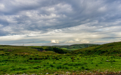 Obraz premium A dramatic cloudy sky with patches of blue over a green mountainous landscape in Meghalaya. 