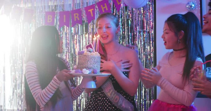Birthday girl receiving cake, blowing candles, wearing ribbon and toasting under fringe backdrop