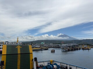A ferry arriving at a bustling port with a majestic volcano or large mountain visible in the...
