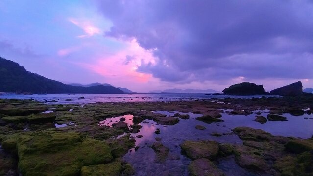 Ethereal morning at Papuma Beach with rugged rocks, soft lavender skies, and mossy tide pools reflecting dramatic clouds capturing nature's beauty in a tranquil coastal scene
