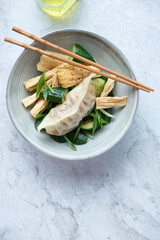 Plate with tofu skin, smashed cucumber salad and pork dumpling, vertical shot on a white stone background with space, flat lay