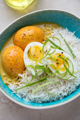 Basmati rice with curried eggs and spring onion served in a turquoise bowl, middle closeup, vertical shot