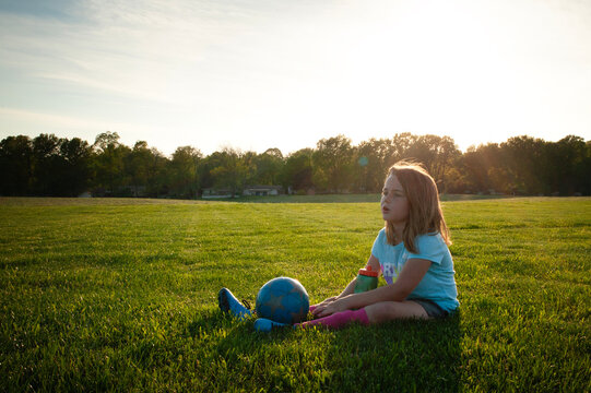 Young girl resting on sidelines with soccer ball and water bottl